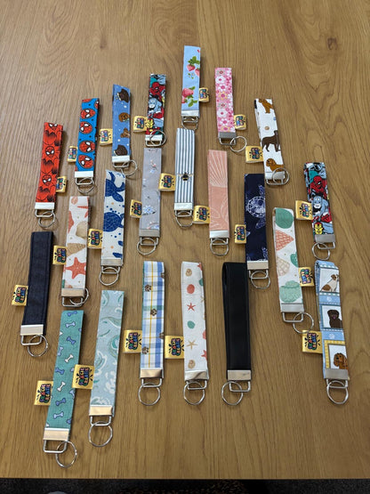 Collection of various patterned keyrings on a wooden surface. All with metal hardware.