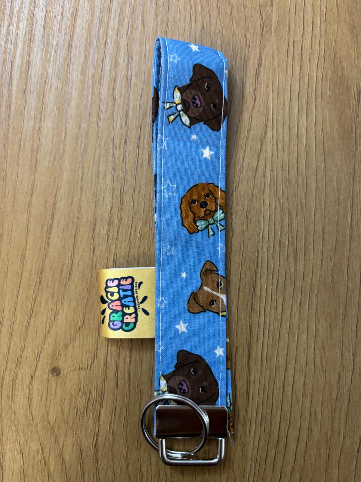 Keychain strap with cartoon dog design on a blue background, attached to a yellow tag, on a wooden surface with metal hardware