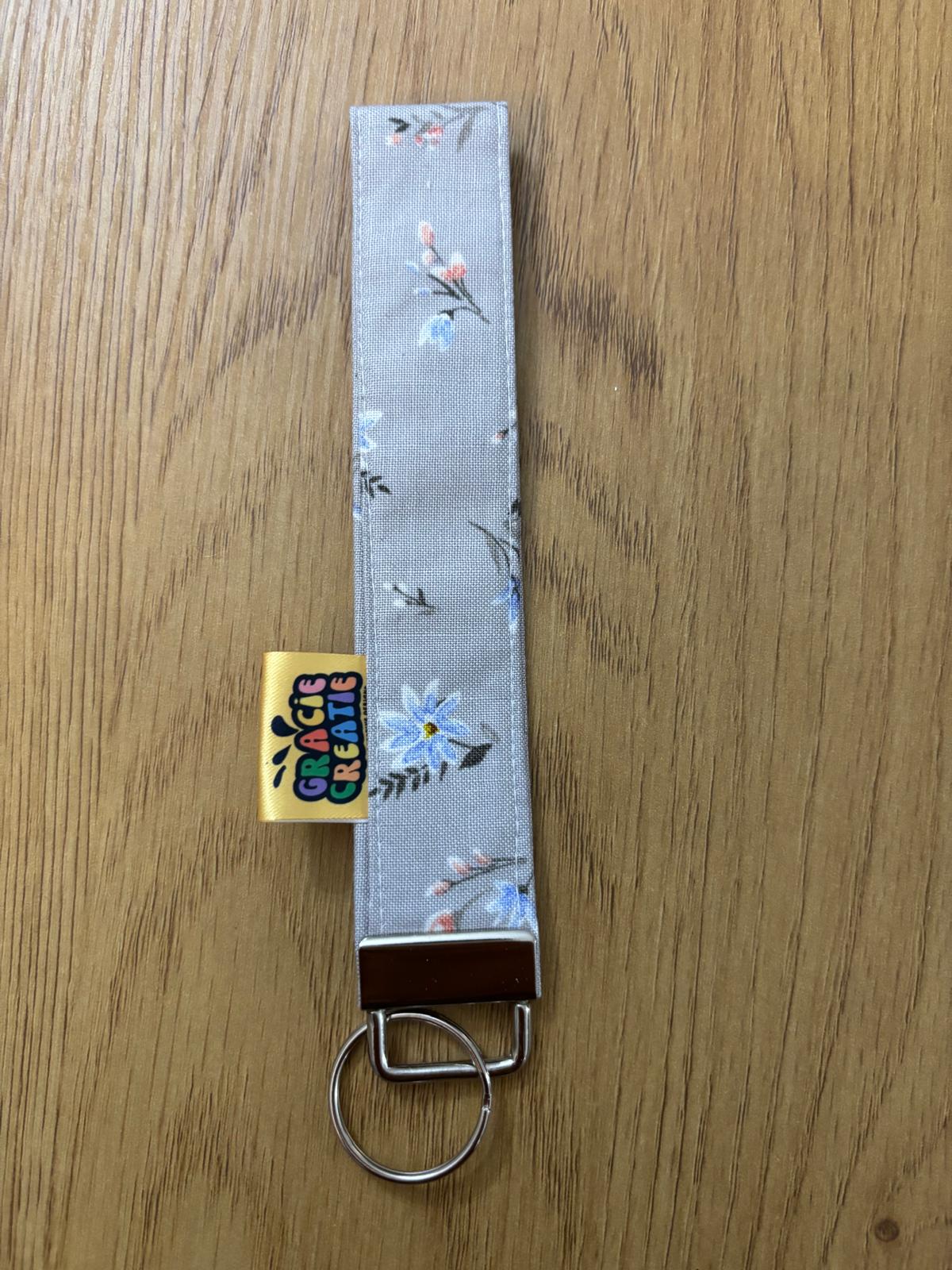 Floral keychain strap with a visible brand label on a wooden surface with metal hardware
