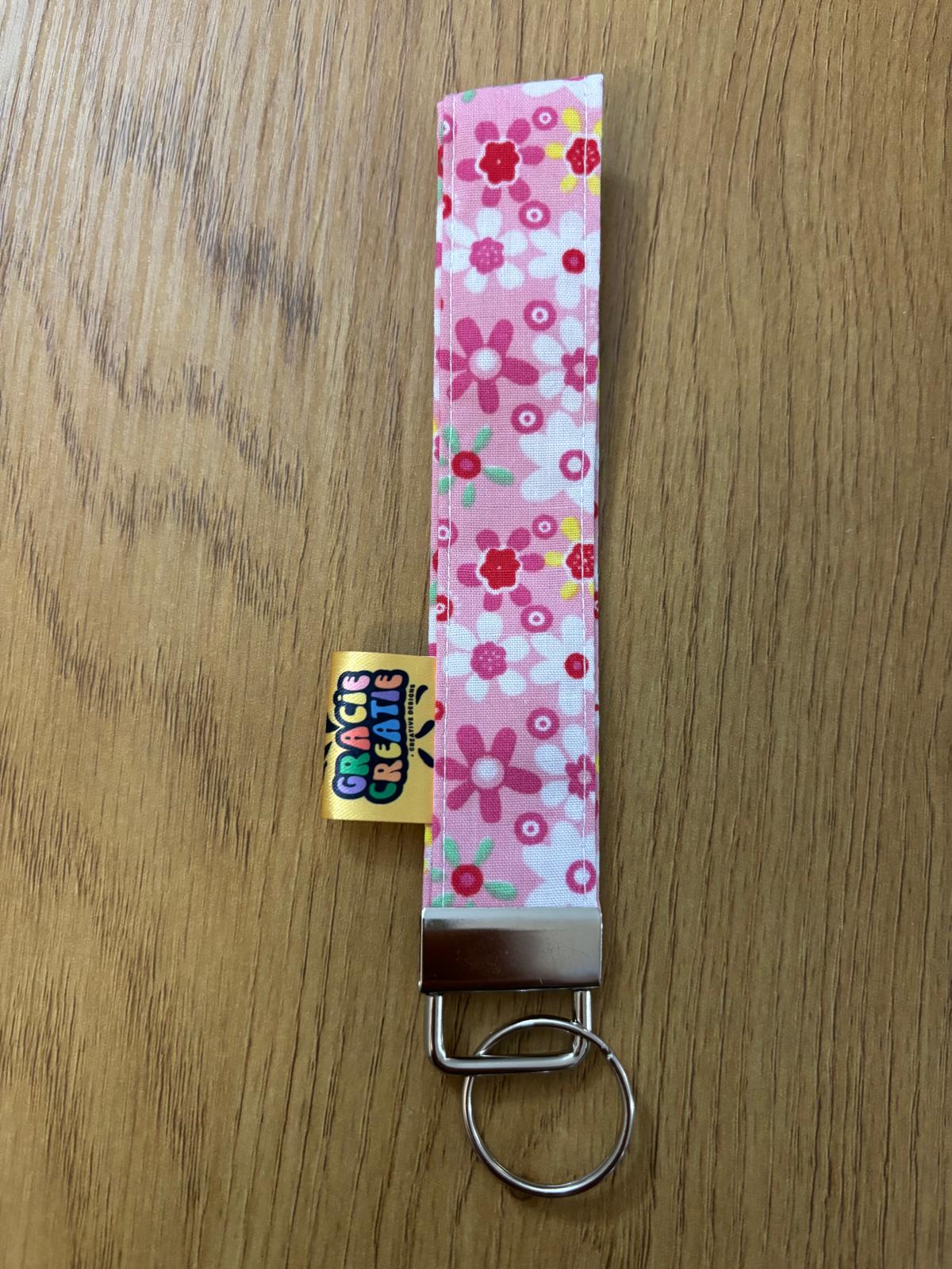 Floral patterned key fob with a visible brand tag on a wooden surface with metal hardware