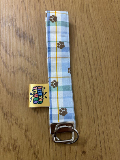 Plaid dog leash with paw prints on a wooden surface, featuring a brand label.