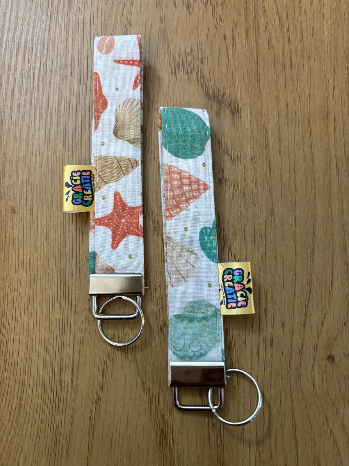 Two keychains with shell and starfish patterns on a wooden surface with metal hardware
