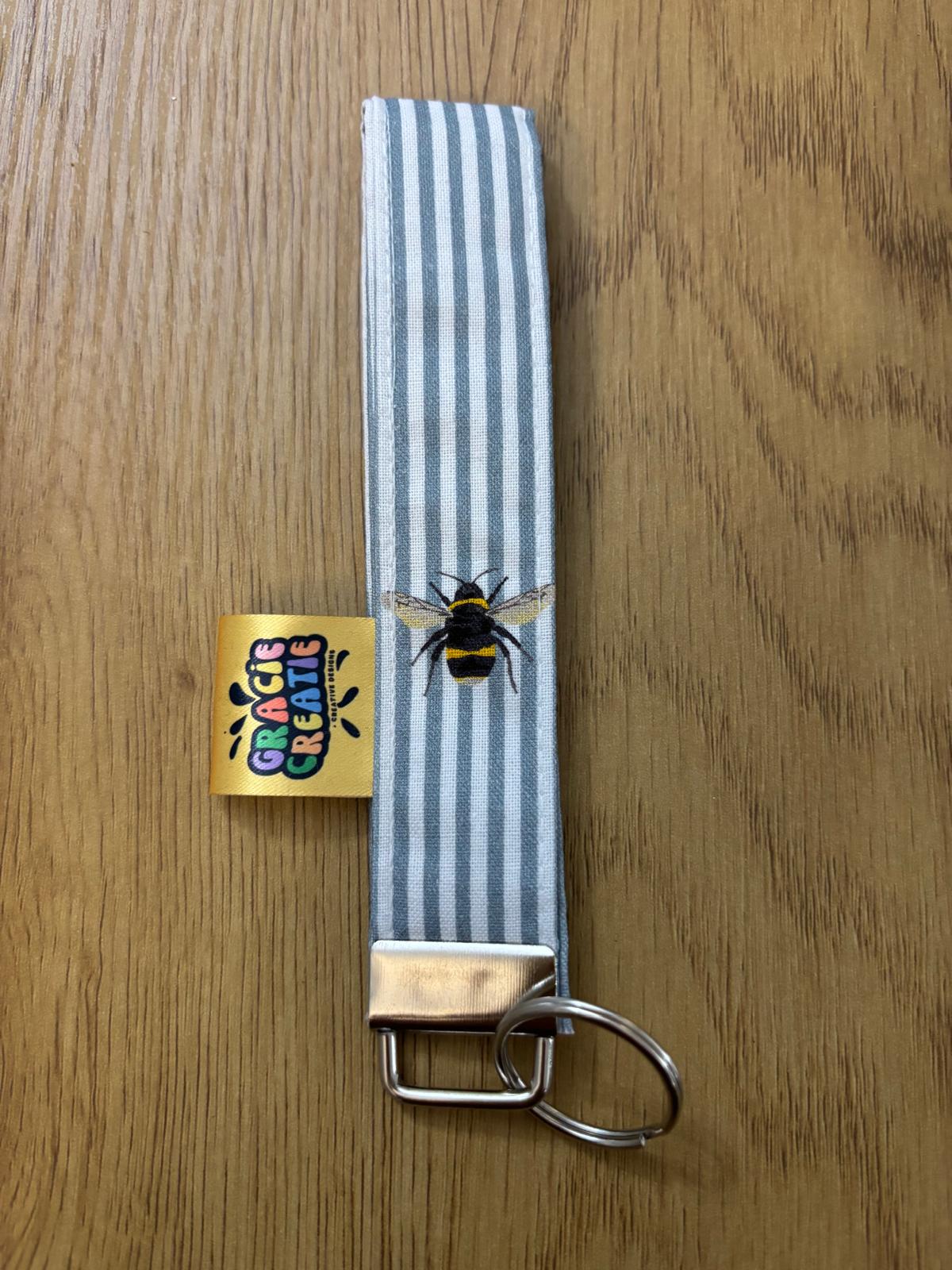Keychain with striped strap and bee design on a wooden surface with metal hardware
