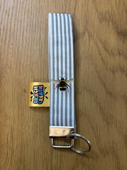 Keychain with striped strap and bee design on a wooden surface with metal hardware